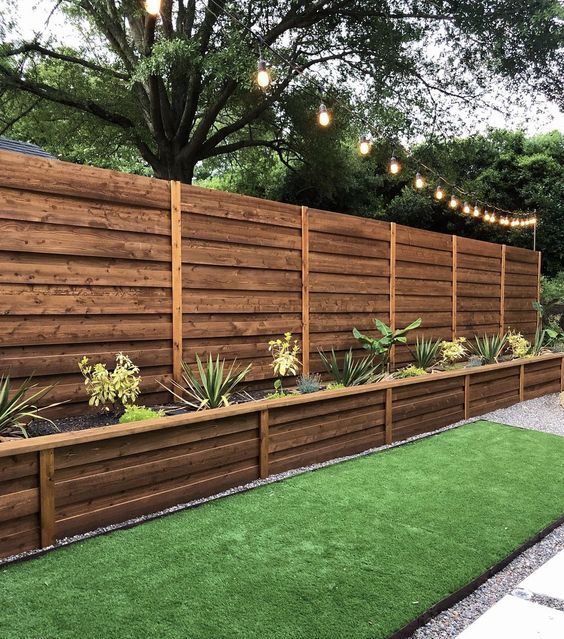 a rich-stained fence paired with a long planter with greenery and blooms are a cool way to get a garden and decorate your fence space