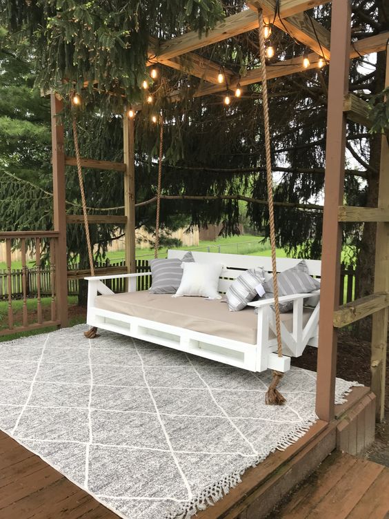 a rustic space with an arbor decorated with lights, a white pallet daybed with pillows is an ideal nook to have a rest here