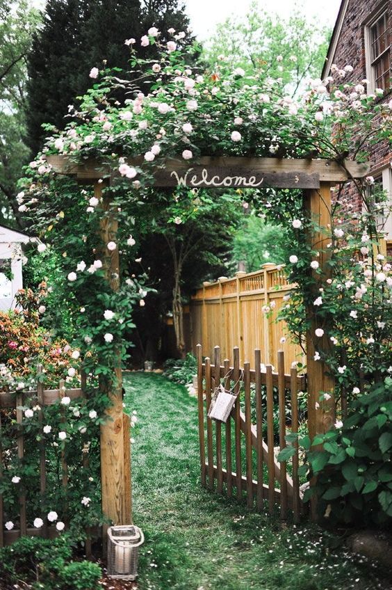 a rustic stained fence paired with a matching gate, with lush blooming climbers on the fence and garden arch are great for a rustic space