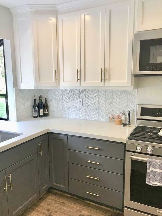 a sage green and white kitchen with white countertops, white chevron tiles on the backsplash and stainless steel appliances