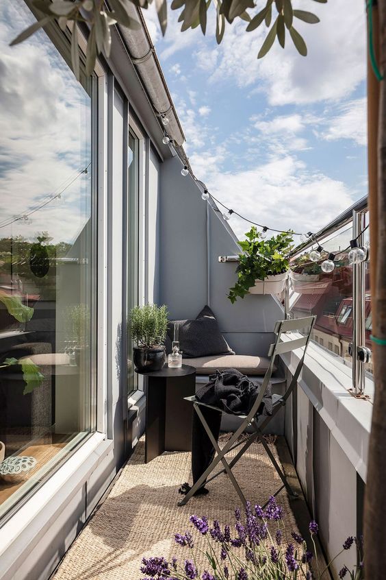 a Scandinavian balcony with a jute rug, a built-in bench, a black table and chair, greenery, lavender and string lights