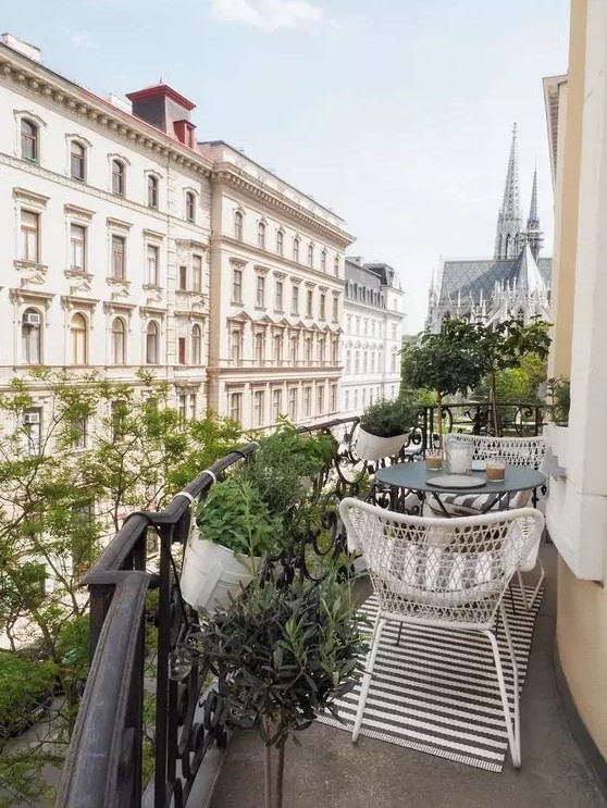 a Scandinavian balcony with a striped rug, white chairs and a black coffee table, potted greenery and fantastic views of Vienna