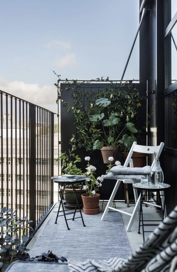 a Scandinavian balcony with folding furniture, a trellis with vines and planters with greenery and blooms is a very chic space