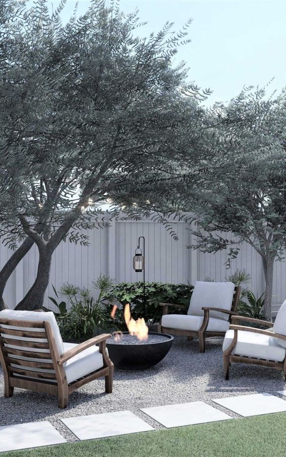 a Scandinavian patio with white chairs, a black fire pit, some trees and greenery around is a cool and lovely spac