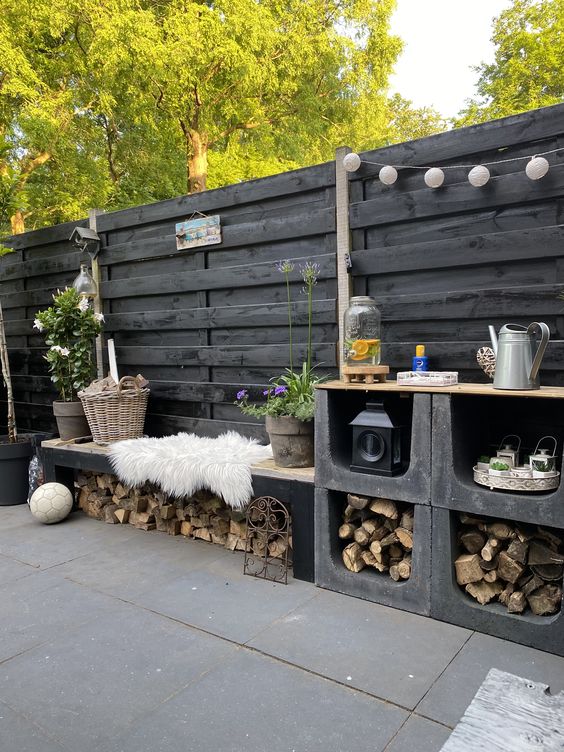 a Scandinavian space with a black fence, a cinder block table and bench with storage, lights and blooms