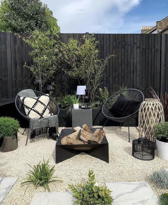 a Scandinavian space with a black fire pit and chairs, a raised garden bed with greenery, candle lanterns and potted greenery to refresh the look