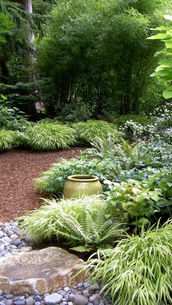 a shady garden with trees, greenery, a gravel and rock path, a vase is a beautiful space, and white blooms refresh it a lot
