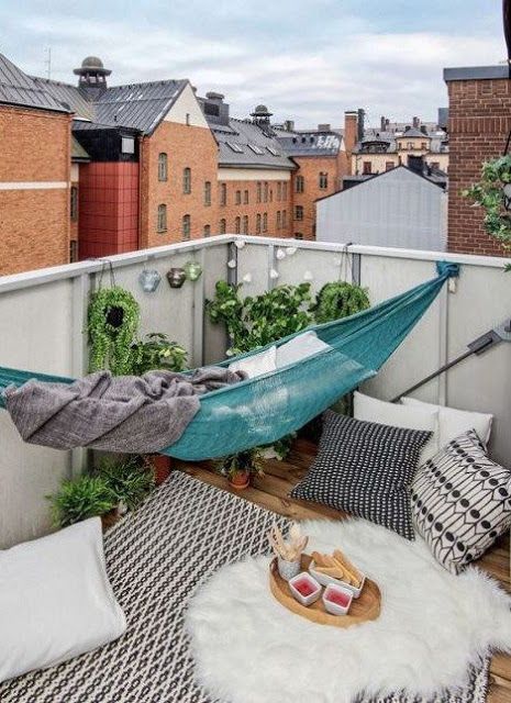 a simple and relaxed boho balcony with a turquoise hammock, boho rugs and pillows, potted greenery, lights and faux fur is amazing