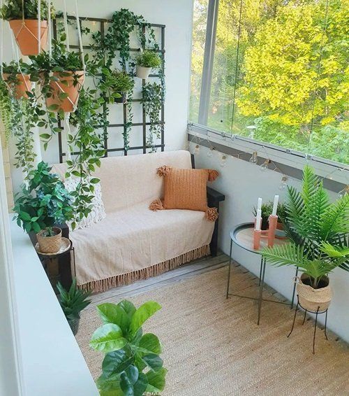 a small and cozy balcony with a loveseat, some pillows, side tables, a rug, potted plants and a trellis with vines and plants attached to it