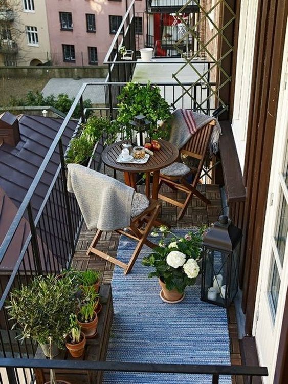 a small and cozy balcony with potted greenery, wooden folding IKEA furniture, potted blooms and candle lanterns