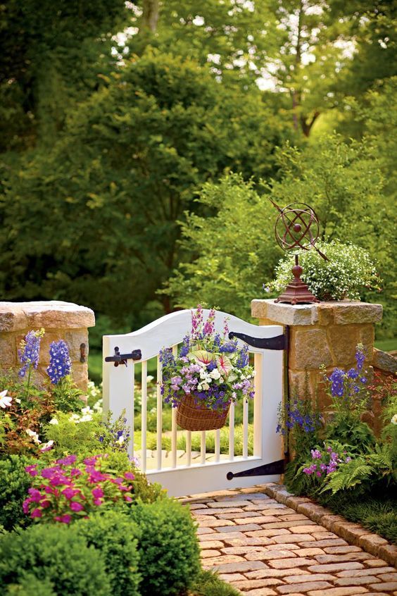 a small and cute garden gate accented with a basket with bright blooms and matching flowers along the path