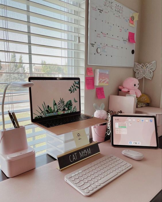 a small and cute workspace with a laptop on a stand, some accessories and devices, decor and a blush table runner