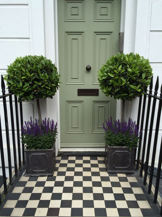 a small and elegant front porch with a sage door, potted topiaries and lavender in the same pots plus a checked tile floor