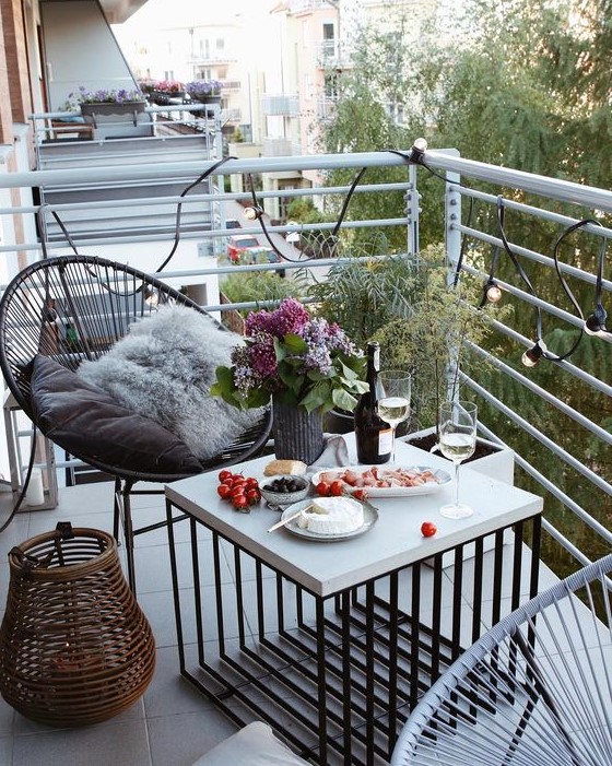 a small and lovely summer balcony with a couple of chairs, a lovely coffee table, a rattan candle lantern and some plants