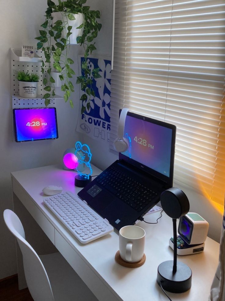 a small and pretty workspace with a laptop on a stand, some neon lamps, a pegboard on the wall and potted greenery