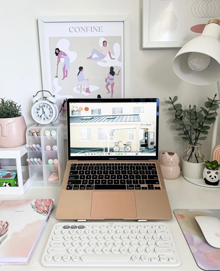 a small and stylish working space with a laptop and some devices, a stand with pens, potted greenery and some accessories and artwork