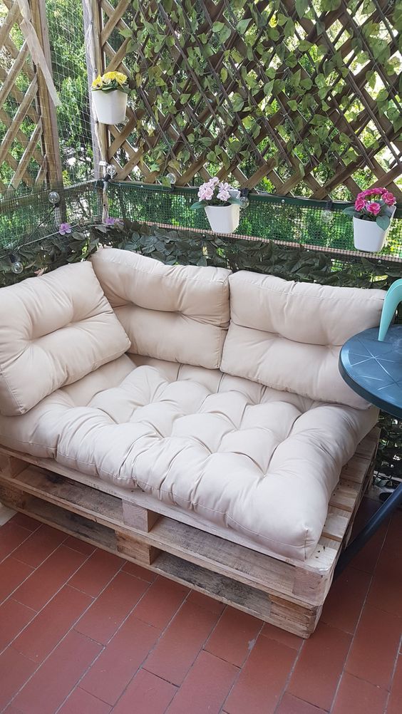 a small balcony with a pallet loveseat, a side table and a trellis that doubles as a privacy screen covered with greenery