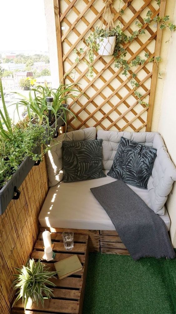 a small balcony with a trellis and some potted plants, a pallet mini sofa and a table, pillows and cushions and a potted plant that covers the trellis