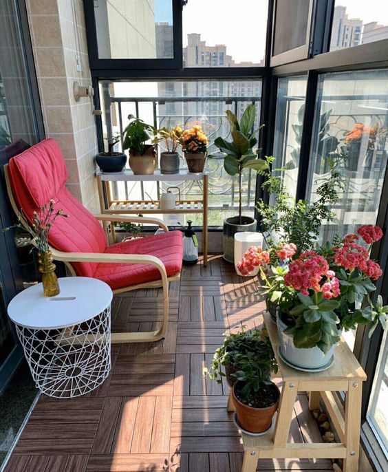 a small balcony with an IKEA chair, a plant stand, lots of potted plants and blooms and a side table is welcoming