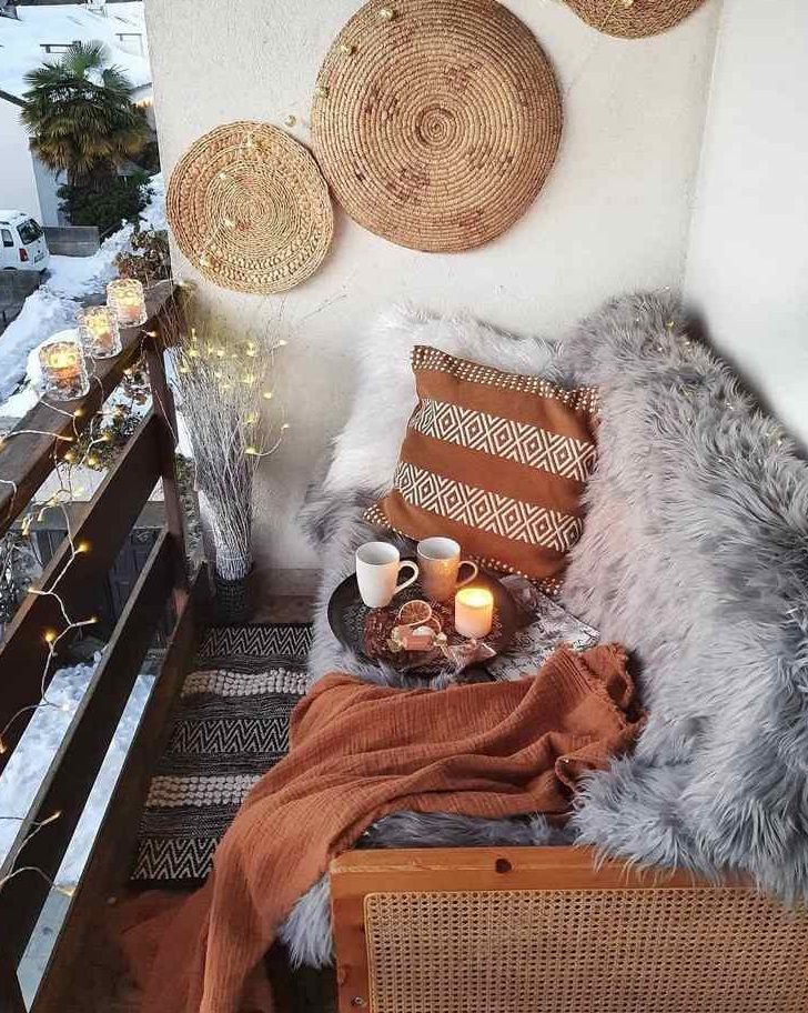 a small boho balcony with a sofa with faux fur, some pillows and blankets, a printed rug and some woden placemats and lights is cool