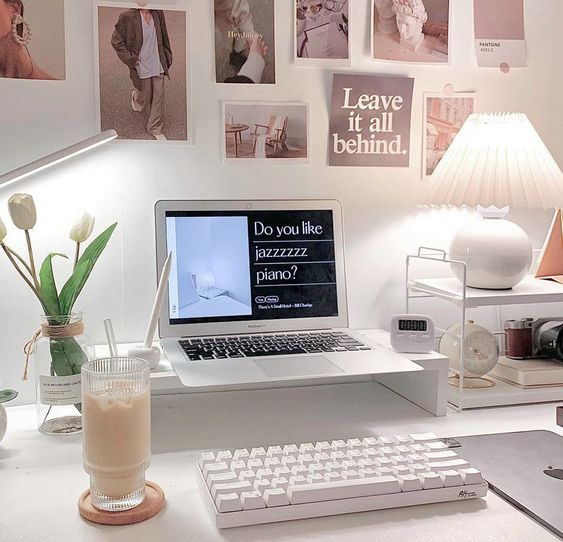 a small modern workspace with a laptop on a stand, a holder with accessories and stuff, a gallery wall and some blooms