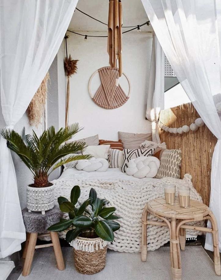 a small neutral boho balcony with a daybed with lots of pillows, some pampas grass and macrame, bamboo, potted plants and a lovely rattan stool