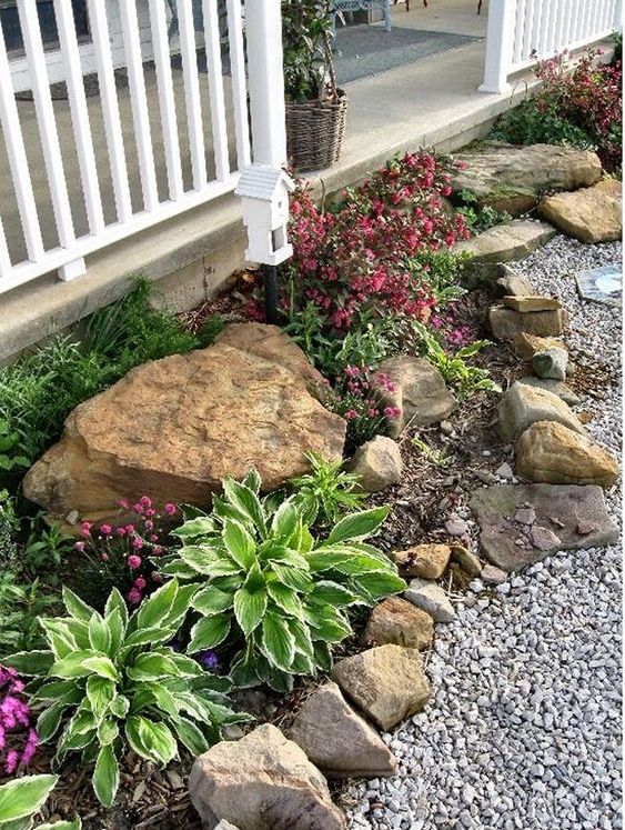 a small rock garden with bright blooms and greenery and a tiny bird house as decor is a cool way to style an edge of your garden