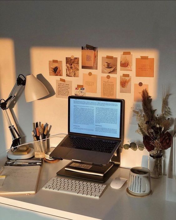 a small study space with a laptop on a stand, a table lamp, a gallery wall of memos