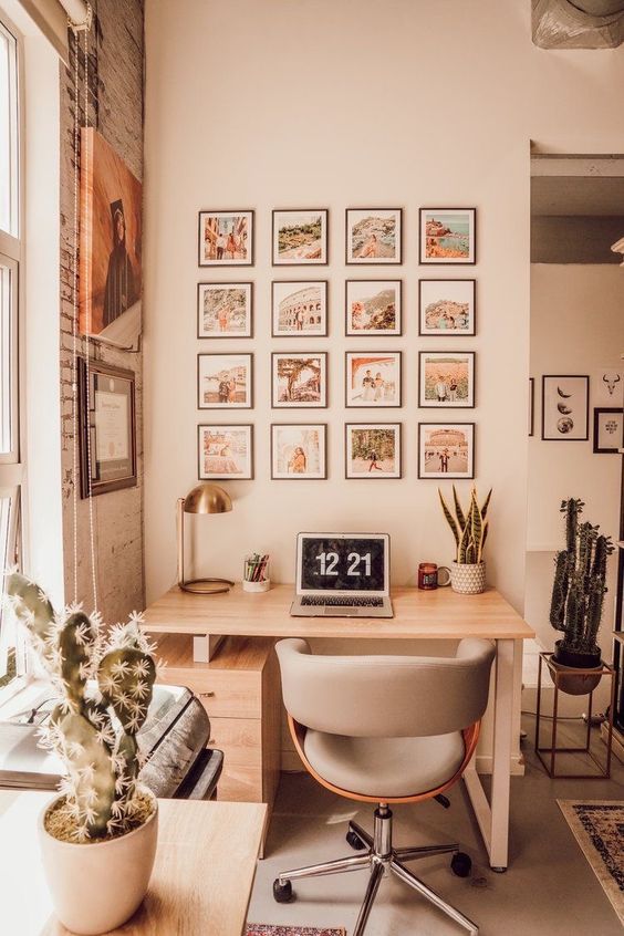 a small welcoming workspace with a desk, a grey chair, a gallery wall and decor, a PC and a table lamp is inviting