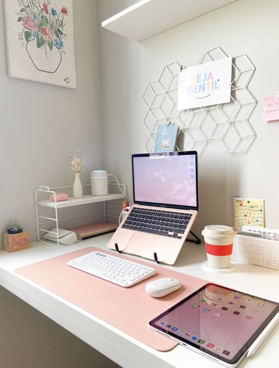 a small workspace with a desk, a stand with various stuff, a laptop and  a grid with a memo, some art and some decor