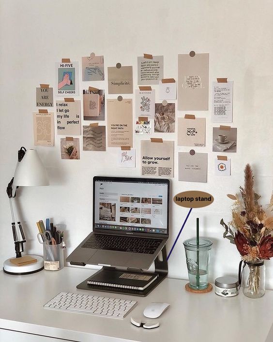 a small yet comfy workspace with a laptop on a stand, a table lamp, a gallery wall with memos and some dried blooms