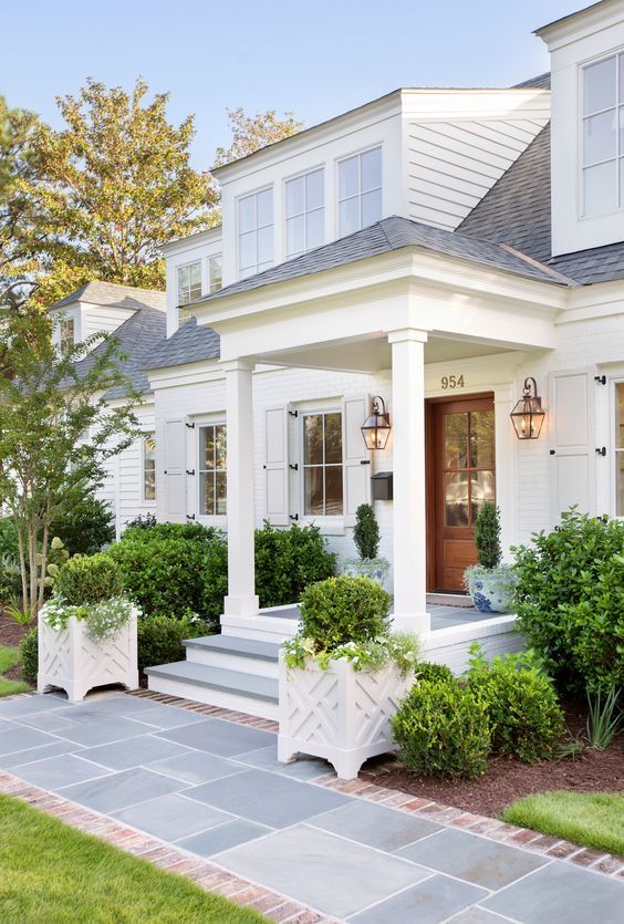 a sophsiticated vintage porch with topiaries, greenery around and chic vintage lamps on the wall