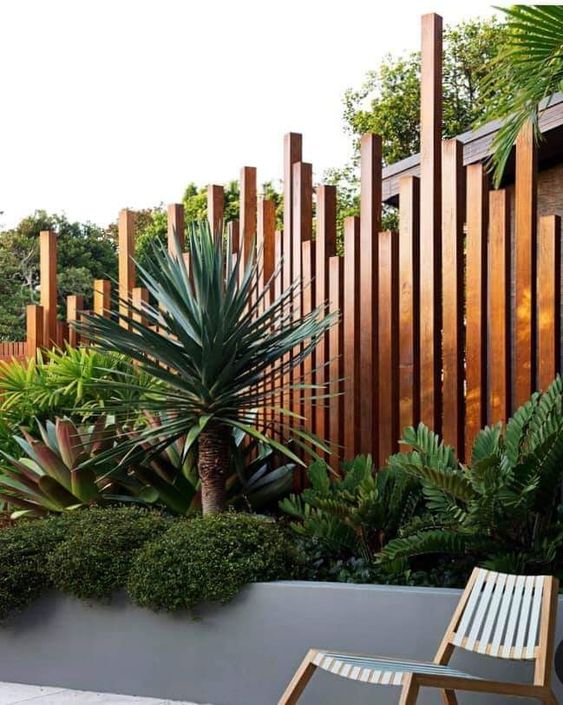 a spectacular stained wooden fence with a unique pattern and a raised garden bed with greenery, oversized agaves and a palm tree
