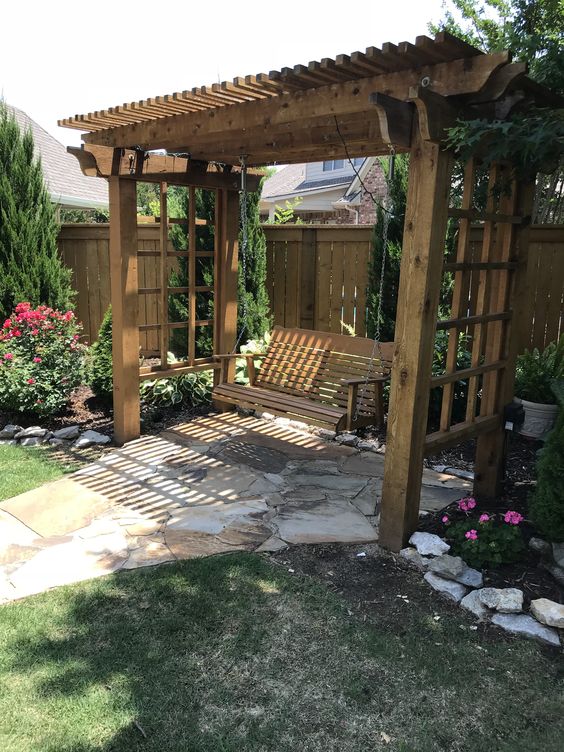 a stained arbor with a pendant bench is a cool idea for a rustic garden, and you may cover the arbor with blooms