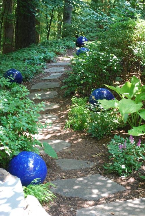 a stone garden path lined up with greenery and bright blue gazing balls for a colorful accent - who needs blooms when you can just place some bright balls