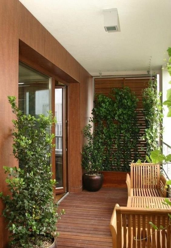 a stylish modern balcony with a stained floor, planked modern outdoor furniture, a planter with a trellis and vines climbing up and some greenery