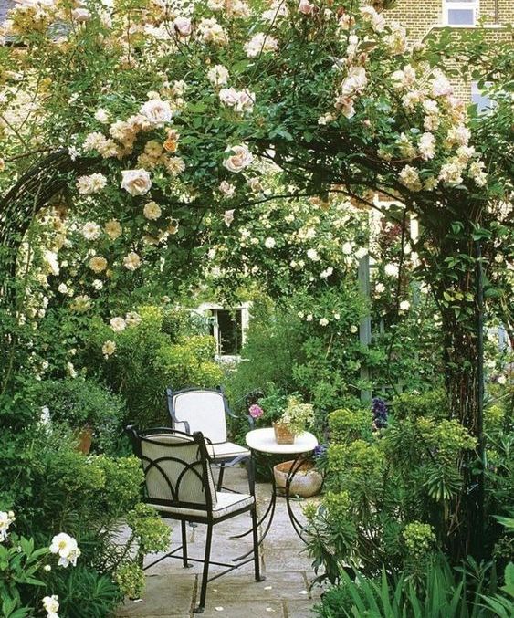 a stylish outdoor space with greenery, two metal arches with blooming vines, refined garden furniture is a lovely space to enjoy the beauty of the space