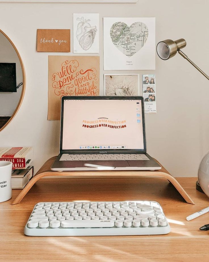 a stylish workspace with a laptop on a stand, a keyboard, a gallery wall, a table lamp plus some books on the desk