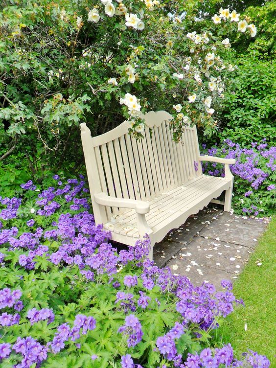 a super colorful garden nook with a white bench, purple and white blooms around is a vintage-inspired blooming space