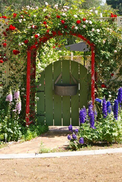 a tall wall trellis, a green gate and a red arbor plus greenery, red and white blooms make up a lovely and bold entrance with a classic color combo