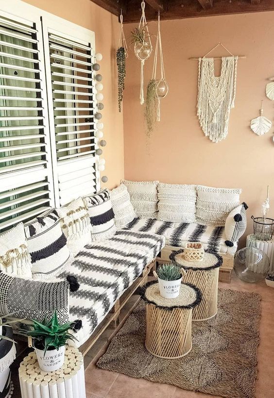 a terracotta-colored balcony with a corner pallet sofa with black and white upholstery, coffee tables and cork tables, macrame and hanging greenery