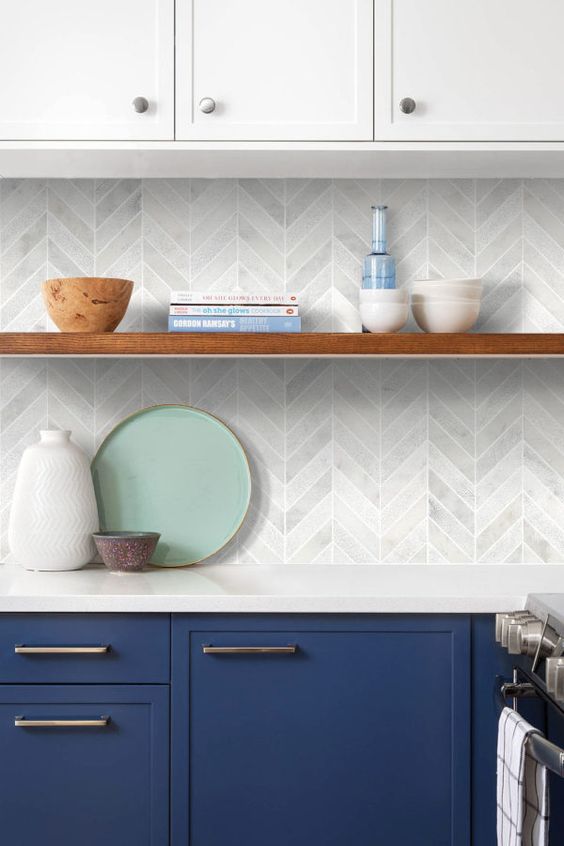 a trendy two-tone kitchen with navy and white cabinets, a marble chevron tile backsplash and some decor