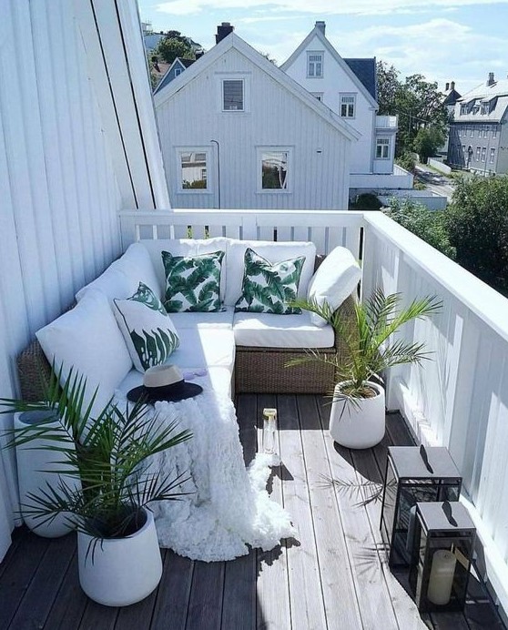 a tropical balcony with a corner bench, potted plants, tropical print pillows, candle lanterns is small yet welcoming