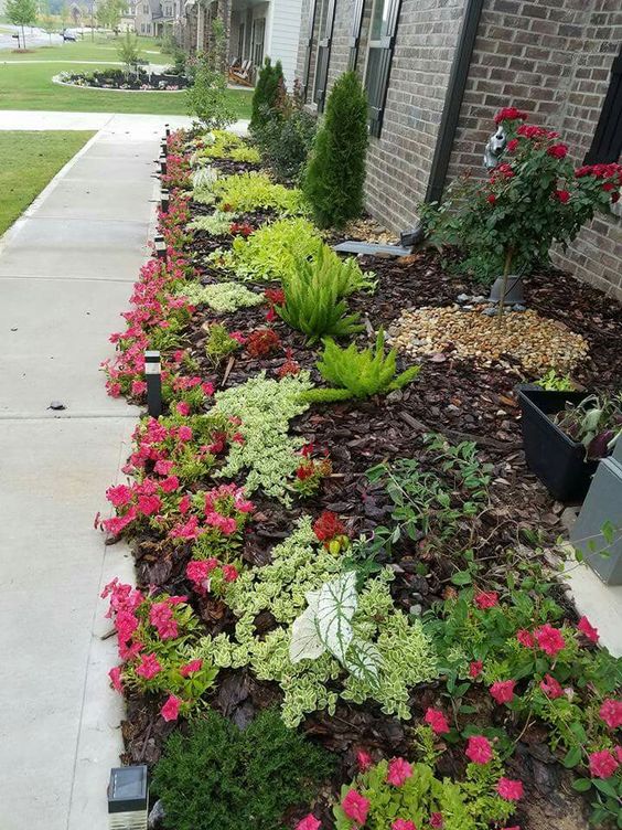 A long flower bed dotted with greenery and bright red flowers plus topiary trees is a stylish addition to the front yard that mathces the brick exterior walls.