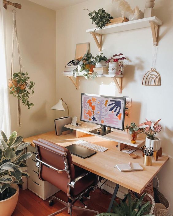 a welcoming and cool workspace with shelves with decor and plants, a desk with a PC and some pens and stuff like that, some more plants and a leather chair