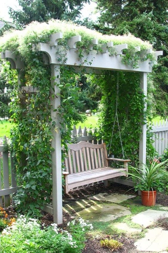 a white arbor covered with greenery, with a swinging vintage bench is a beautiful solution for a refined garden