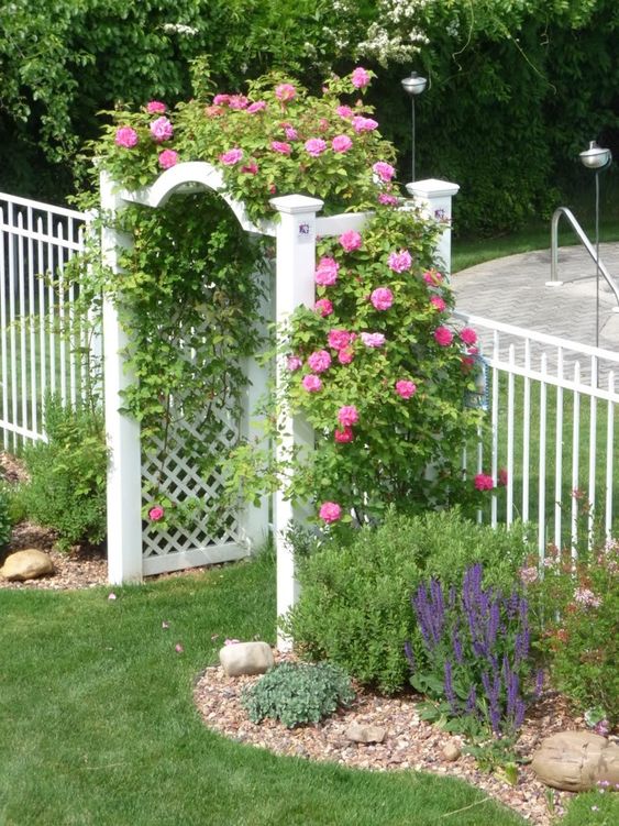 a white creatively shaped trellis arbor is done with greenery and pink blooms is a beautiful idea for a vintage-inspired space