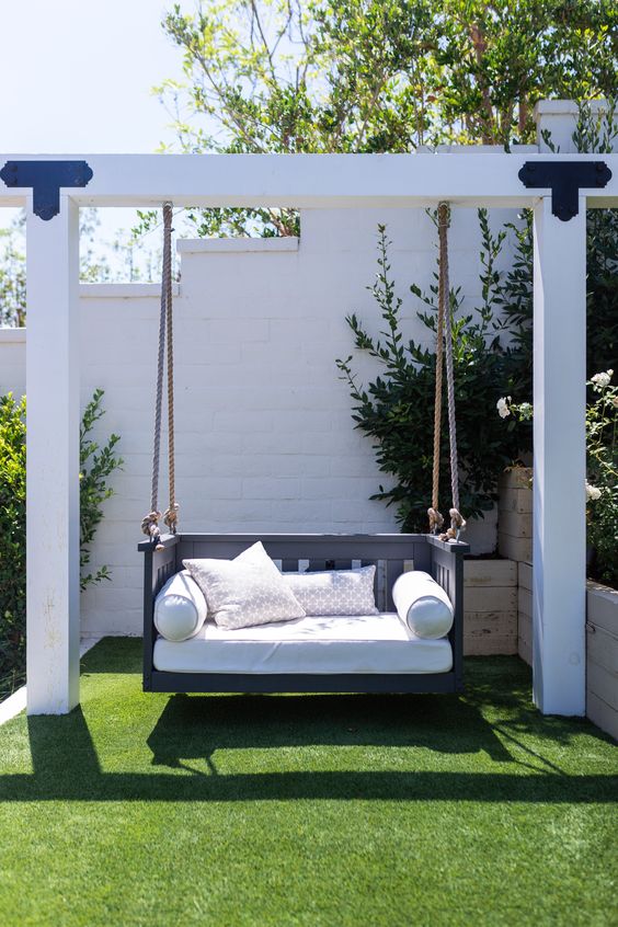 a light-colored frame with a black swing chair and pillows is a cool idea for a modern or Scandinavian garden or backyard