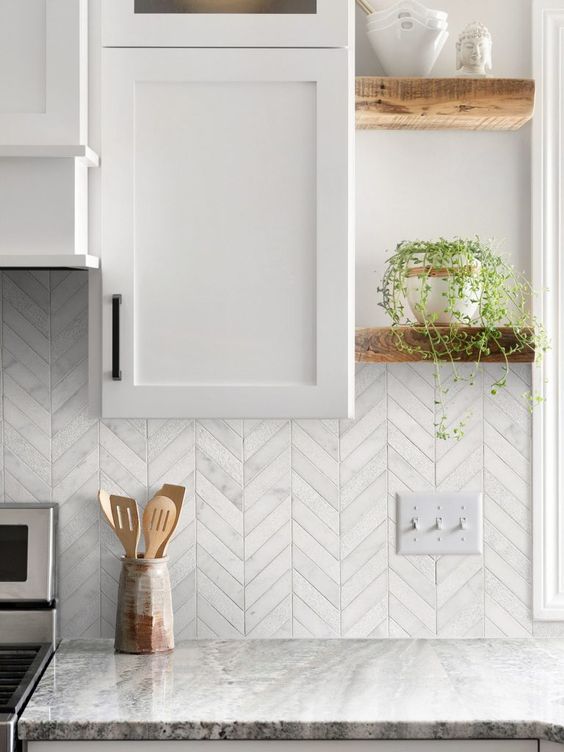 a white kitchen with shaker cabinets, grey stone countertops, stained shelves and some greenery is amazing