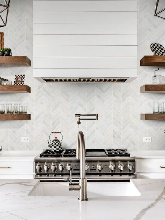 a white modern farmhouse kitchen with a grey marble chevron backsplahs and stained shelves, a planked hood